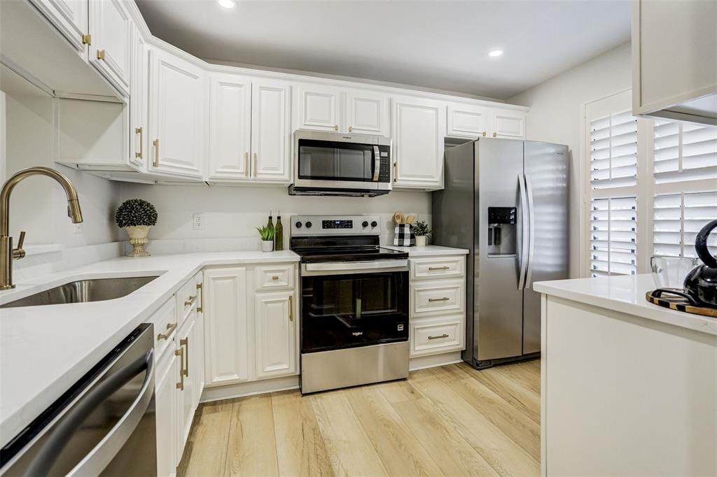 A kitchen features white cabinets, stainless steel appliances, light wood floors, and white countertops — 460 S PAULA DRIVE UNIT 402, DUNEDIN, FL