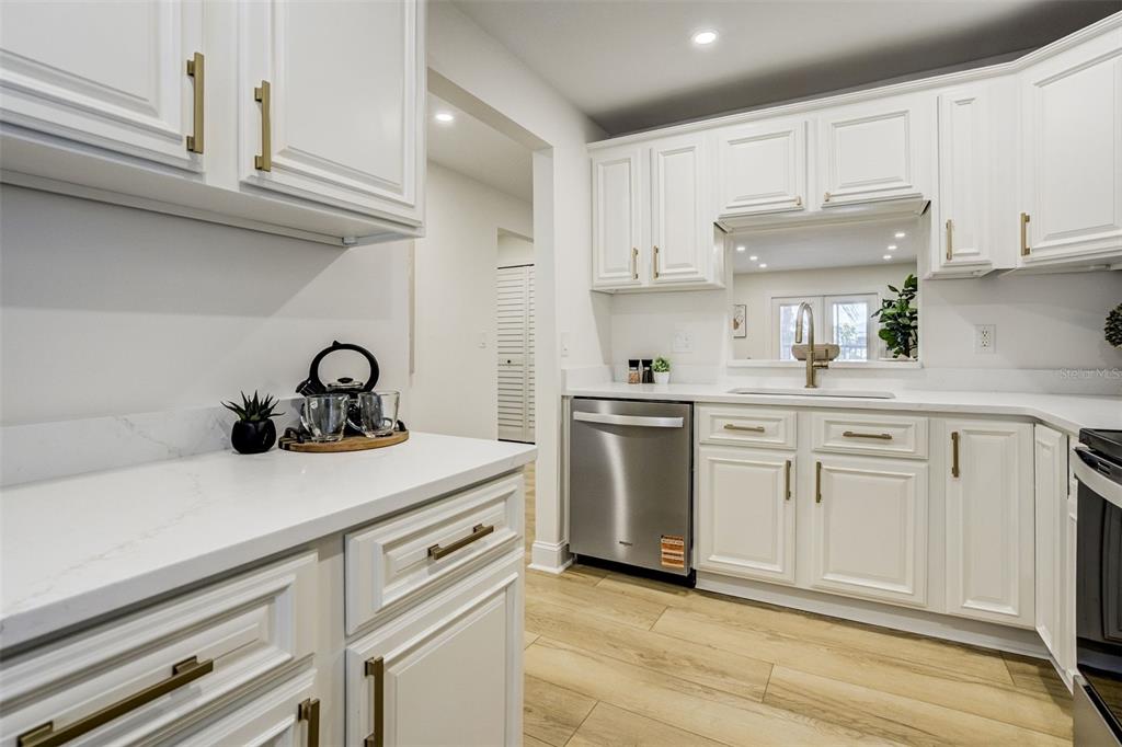 A kitchen with white cabinets, gold hardware, stainless steel appliances, and light wood-look flooring — 460 S PAULA DRIVE UNIT 402, DUNEDIN, FL