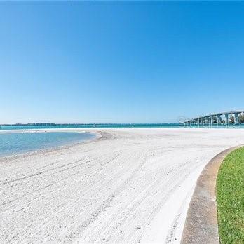 A wide, white sand beach meets the water with a bridge visible in the distance — 830 S GULFVIEW BOULEVARD UNIT 501, CLEARWATER BEACH, FL
