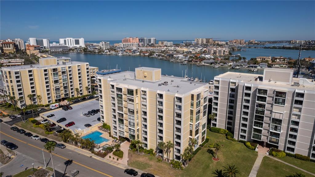 An aerial view shows three multi-story apartment buildings with a swimming pool and parking lot — 830 S GULFVIEW BOULEVARD UNIT 501, CLEARWATER BEACH, FL