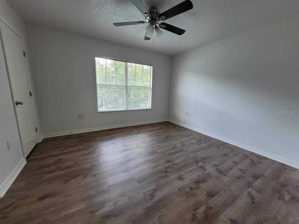 An empty bedroom features light gray walls, wood-look flooring, a ceiling fan, and a window — 2348 SW 42ND DRIVE UNIT 148, GAINESVILLE, FL