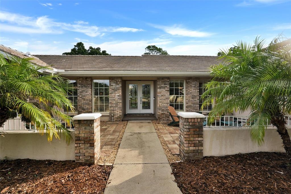 A brick house exterior features a paved walkway leading to a double-door front entrance — 7913 BROADMOOR PINES BOULEVARD, SARASOTA, FL