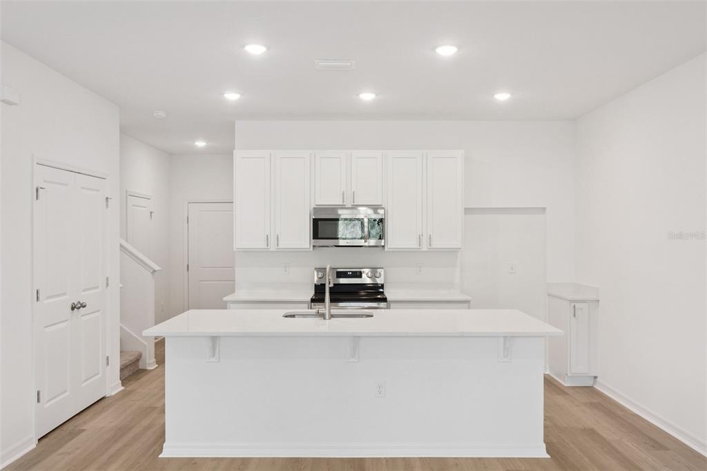 A modern kitchen features white cabinets, a central island, and light wood-look flooring — 2278 RED PINE COURT, EUSTIS, FL