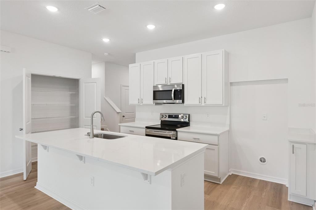 A modern kitchen features white cabinets, a large island with a sink, and stainless appliances — 2278 RED PINE COURT, EUSTIS, FL