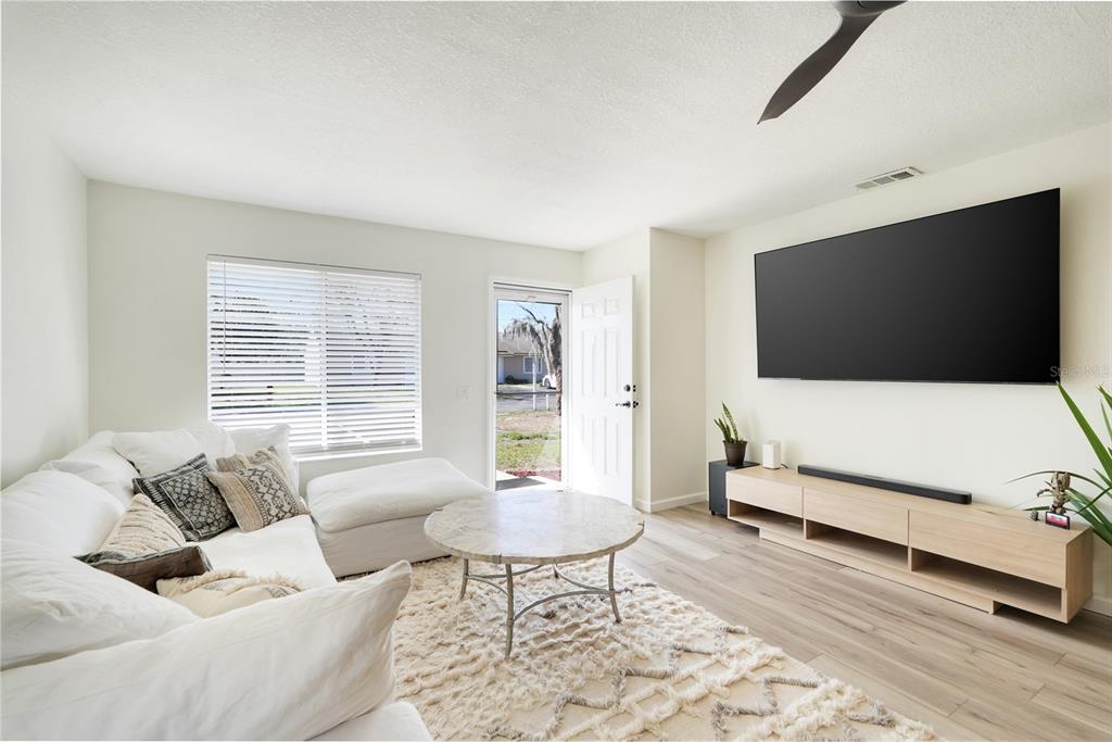 A living room features a white sectional sofa, a round coffee table, and a wall-mounted television — 30024 TAVARES RIDGE BOULEVARD UNIT 62, TAVARES, FL