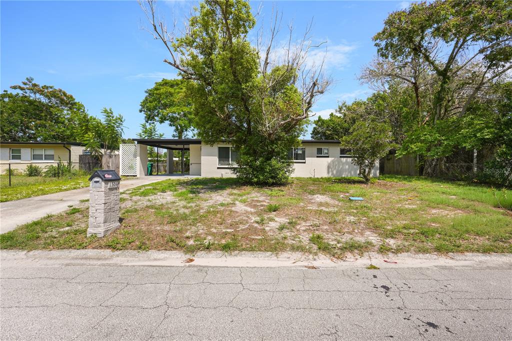 A single-story house with a carport and a large tree in the front yard — 1506 HARVARD DRIVE, COCOA, FL