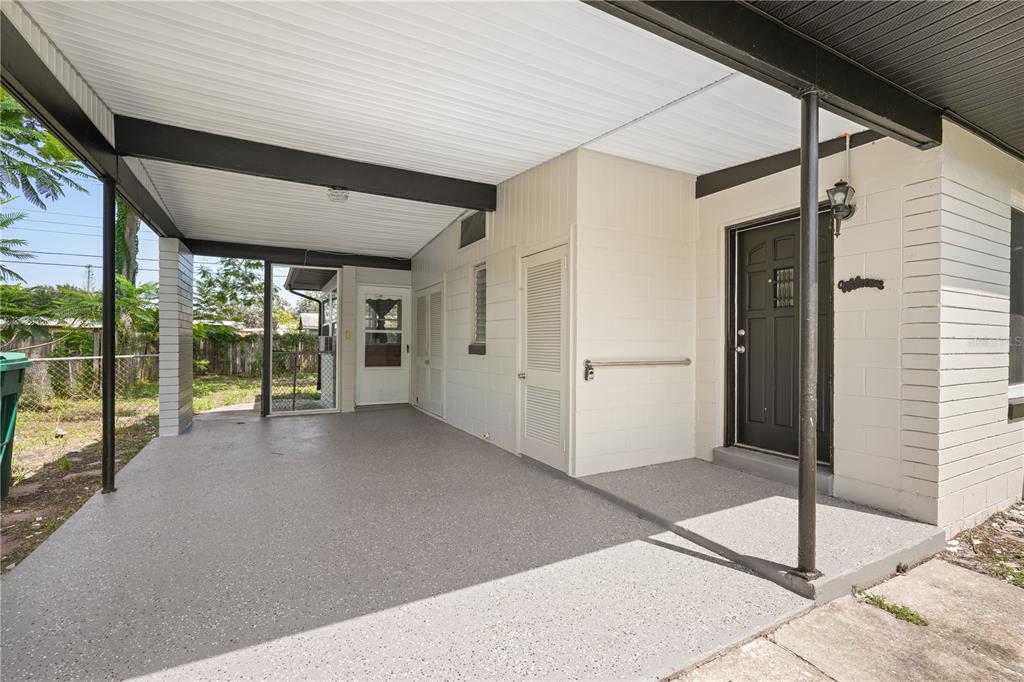 A covered carport with a concrete floor leads to a black front door and storage closets — 1506 HARVARD DRIVE, COCOA, FL