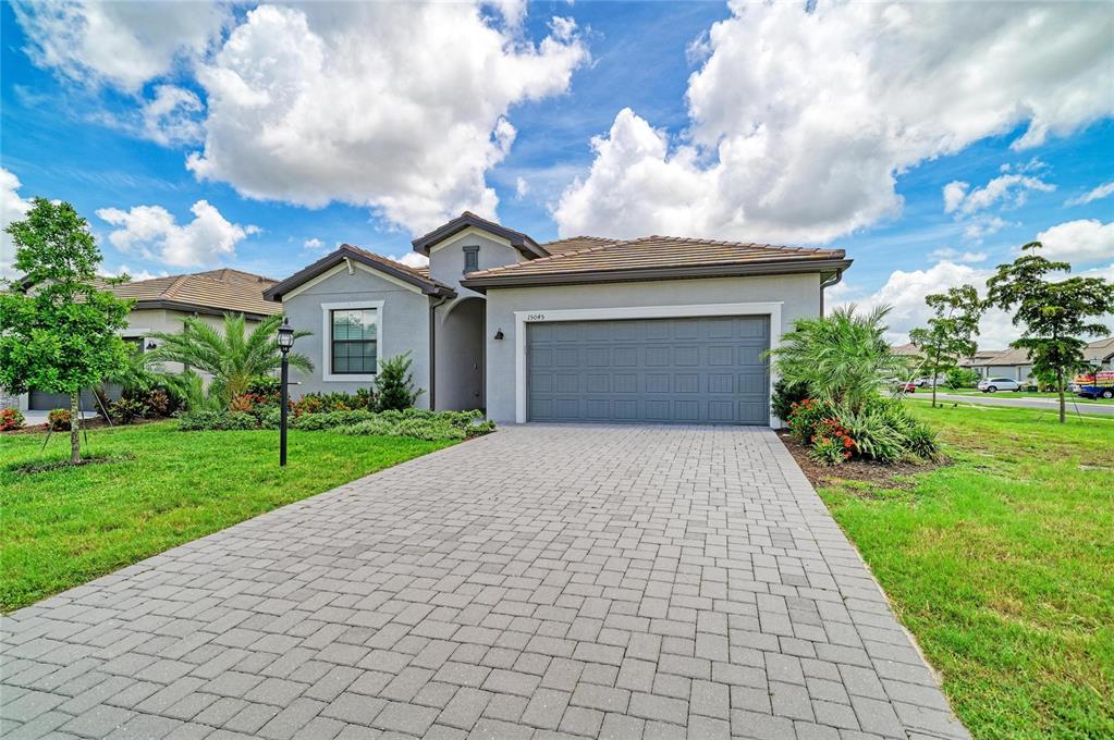 A single-story house with a gray stucco exterior, a tiled roof, and a paver driveway — 15045 SERENE SHORES LOOP, BRADENTON, FL