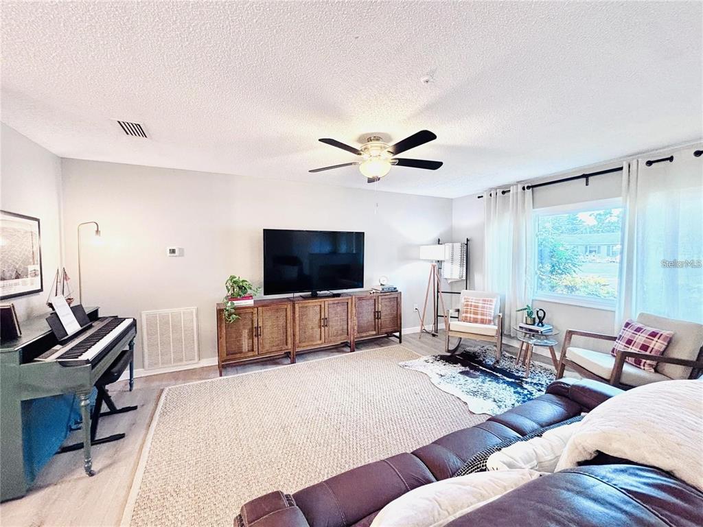 A living room features a piano, a television on a wooden console, and two armchairs — 4033 13TH AVENUE W, BRADENTON, FL