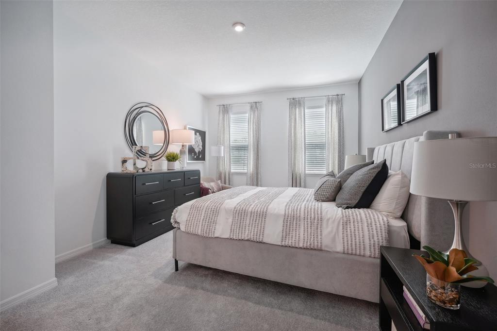 A bedroom features a gray upholstered bed, a dark dresser, and two windows with curtains — 23603 GRINDSTONE WAY, SORRENTO, FL