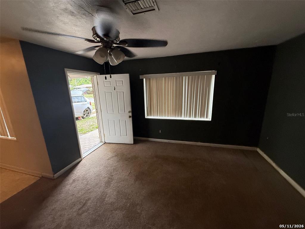 A room with dark walls, brown carpet, a ceiling fan, and an open exterior door — 2715 DIXIE ROAD, LAKELAND, FL