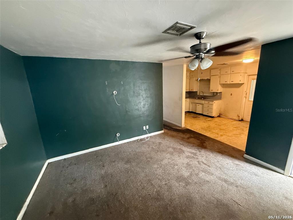 A living room with dark green walls and carpet leads into a kitchen with cabinets — 2715 DIXIE ROAD, LAKELAND, FL
