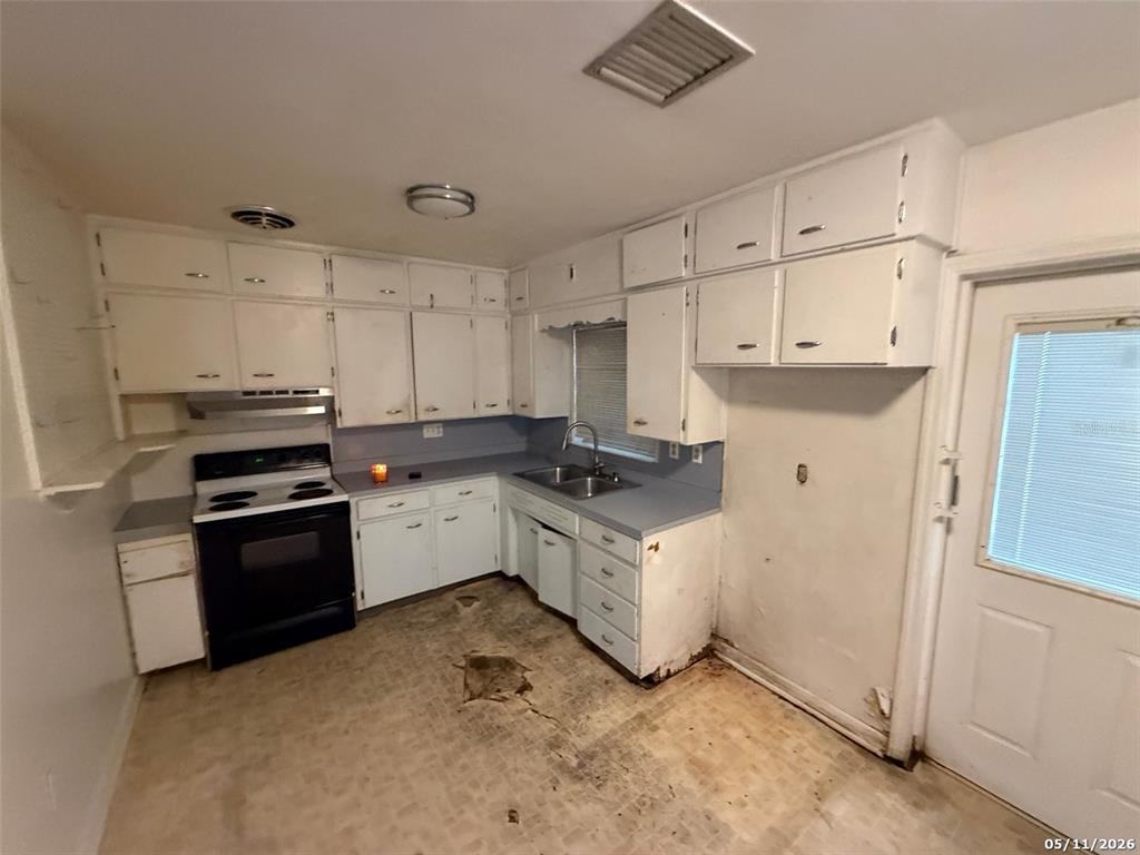 A kitchen features white cabinets, a black stove, a sink, and damaged flooring — 2715 DIXIE ROAD, LAKELAND, FL