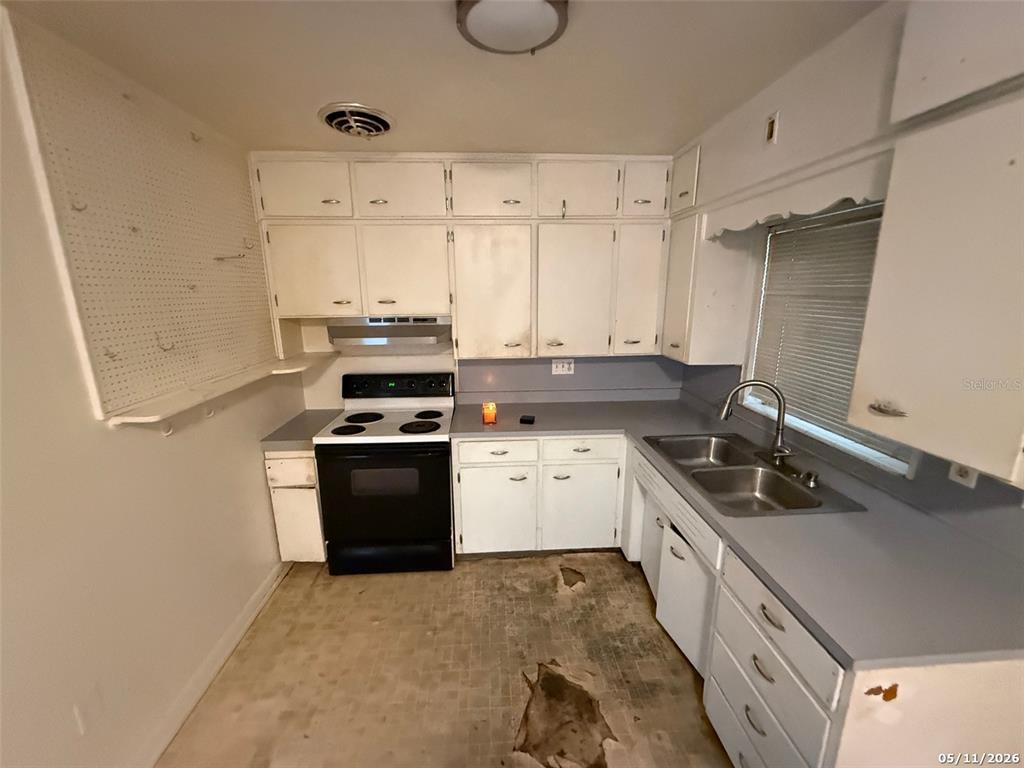 A kitchen with white cabinets, a black stove, a double sink, and damaged flooring — 2715 DIXIE ROAD, LAKELAND, FL