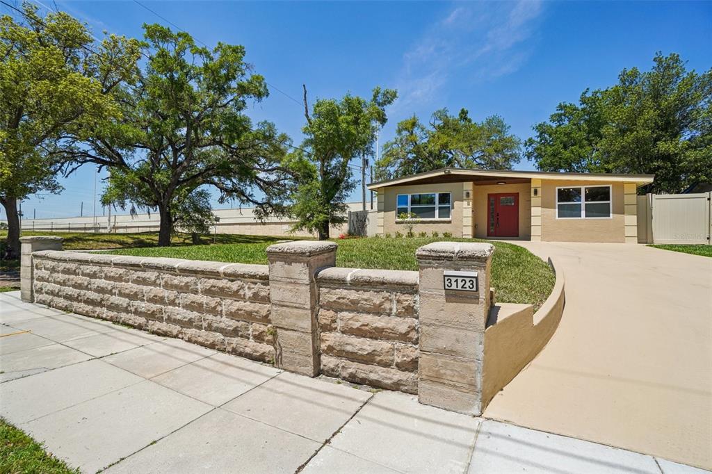 A single-story house with a red front door and a stone wall along the sidewalk — 3123 W LA SALLE STREET, TAMPA, FL
