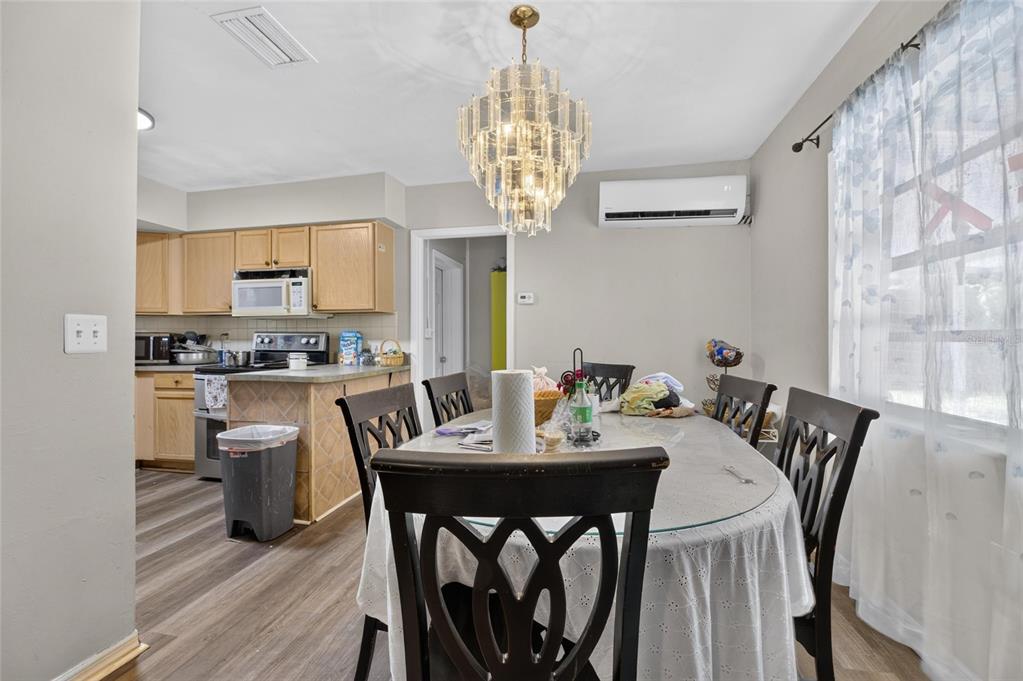 A dining area with a glass table, chandelier, and adjacent kitchen with light wood cabinets — 202 9TH STREET NE, RUSKIN, FL