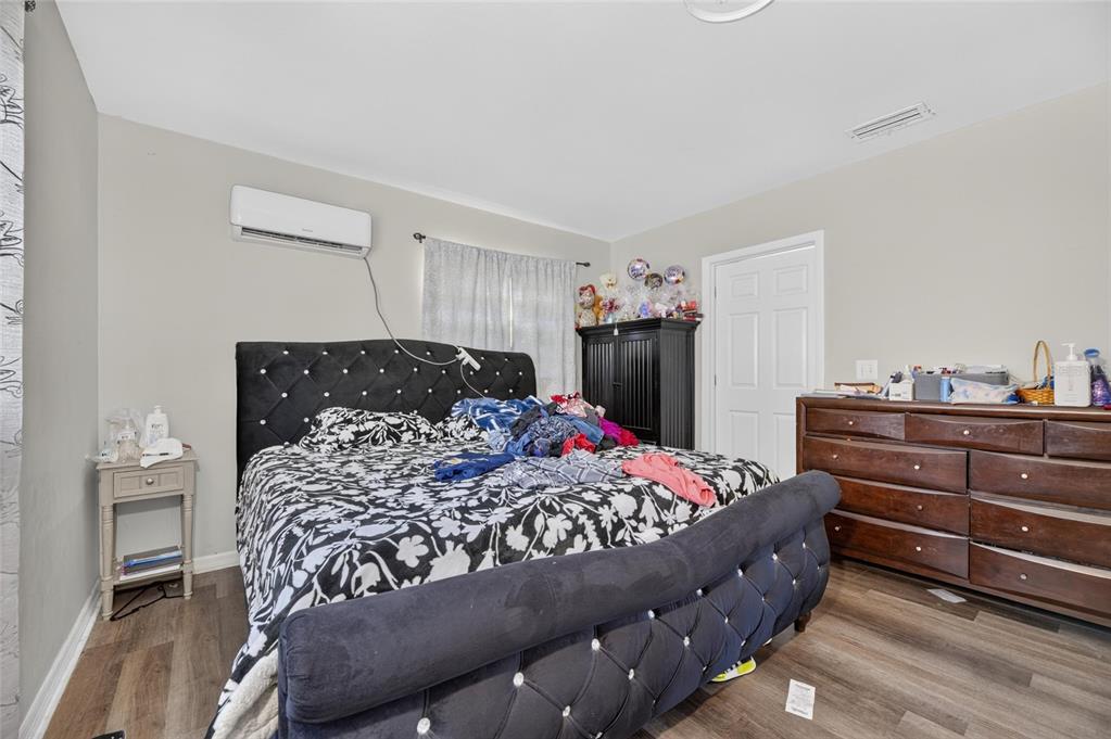A bedroom features a tufted black bed, wood-look flooring, a dresser, and a wall-mounted air conditioner — 202 9TH STREET NE, RUSKIN, FL