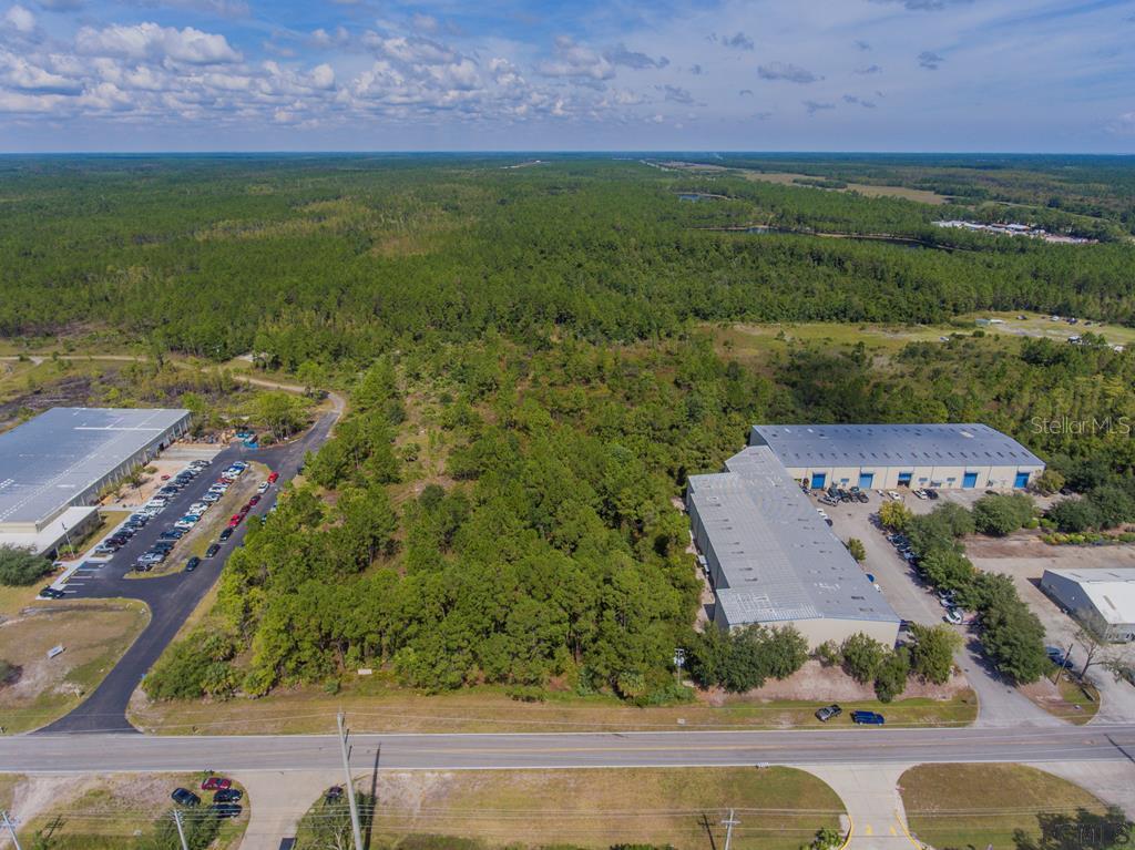 An aerial view shows a wooded lot situated between two industrial warehouse buildings and a road — 26 HARGROVE GRADE UNIT 2, PALM COAST, FL