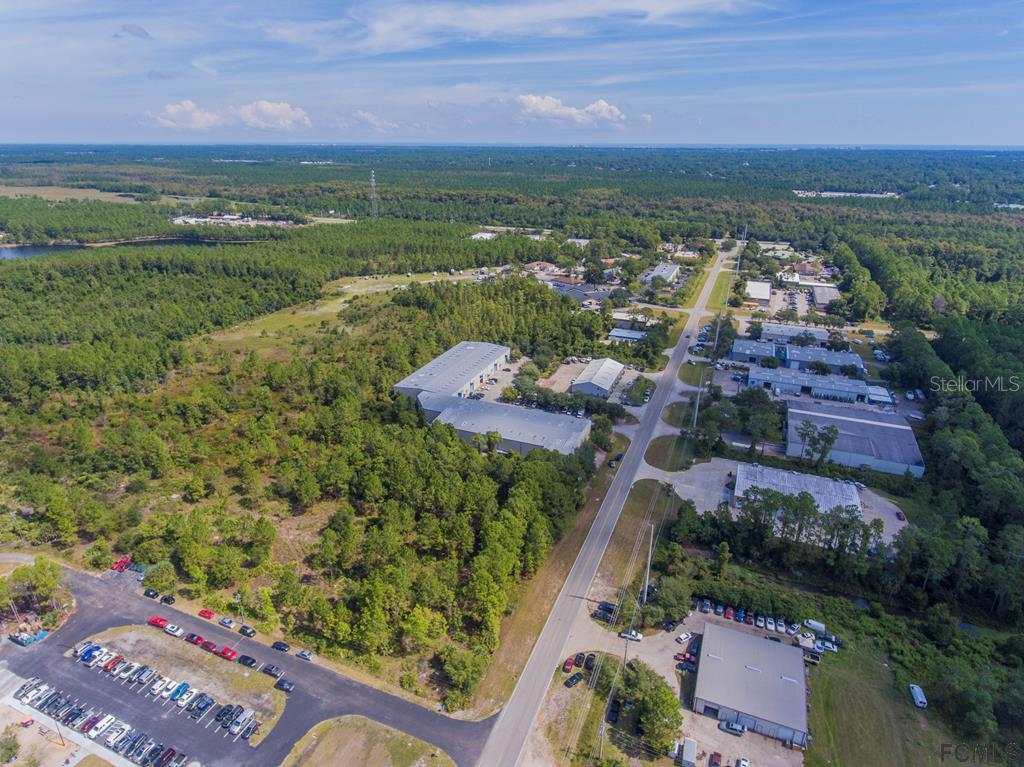 An aerial view shows industrial buildings, parking lots, and surrounding forest under a blue sky — 26 HARGROVE GRADE UNIT 2, PALM COAST, FL