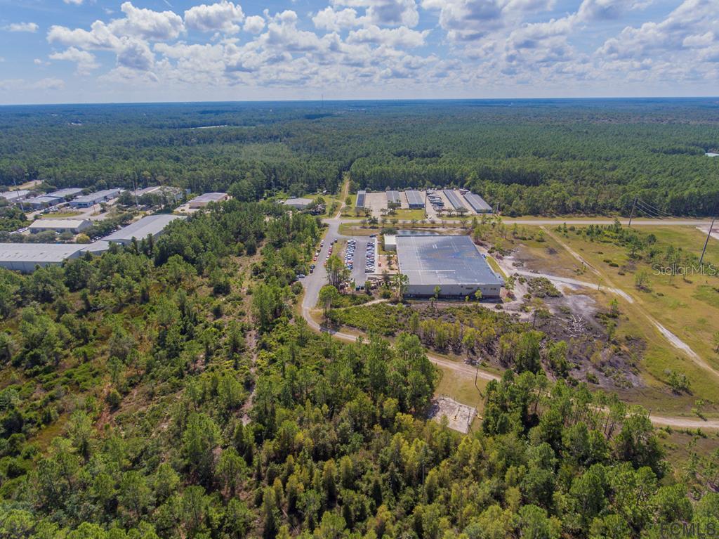 An aerial view shows a large industrial warehouse building surrounded by forest and parking areas — 26 HARGROVE GRADE UNIT 2, PALM COAST, FL