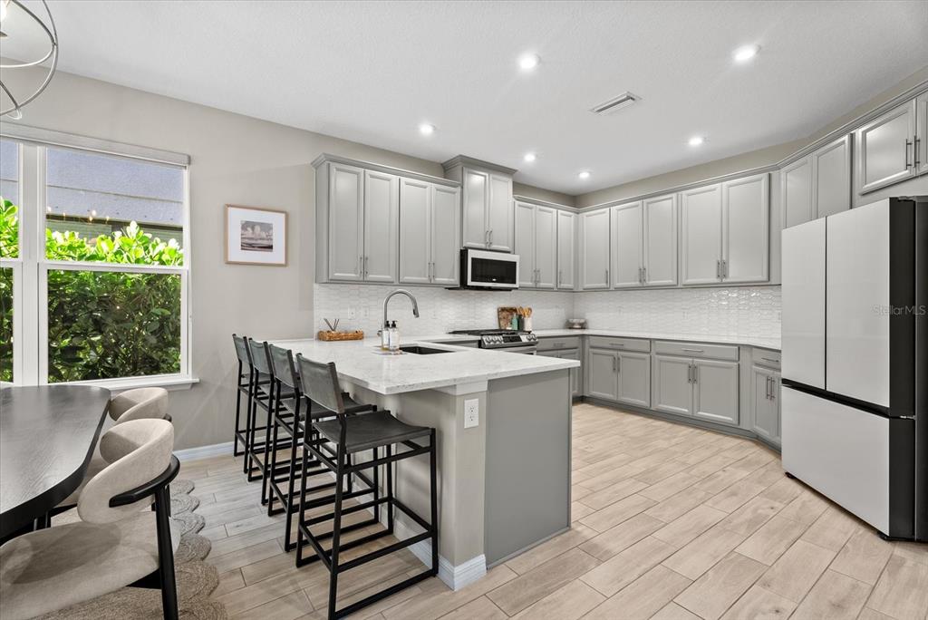 A kitchen features gray cabinets, a white quartz island with bar seating, and wood-look tile flooring — 15360 ISLA PALMA LANE, NOKOMIS, FL
