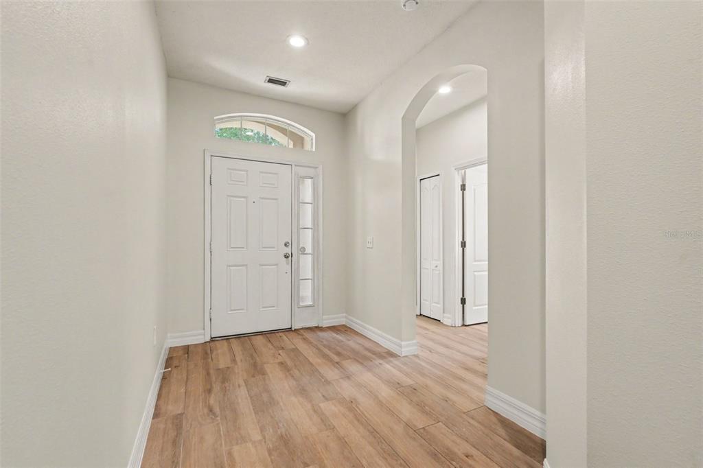 An entryway with light wood-look flooring, a white front door, and an arched hallway opening — 453 WESTCHESTER HILLS LANE, VALRICO, FL