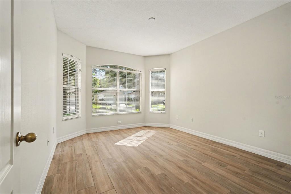 An empty room with light wood-look flooring, beige walls, and a bay window — 453 WESTCHESTER HILLS LANE, VALRICO, FL