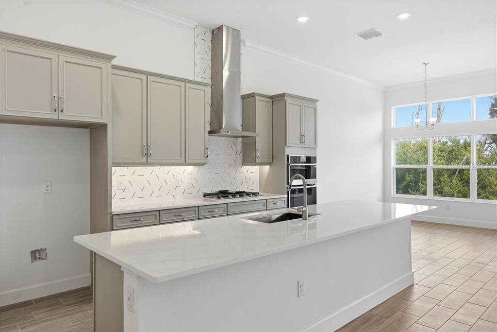 A modern kitchen features light gray cabinets, a white quartz island, and a tile backsplash — 911 SIGNET DRIVE, APOLLO BEACH, FL