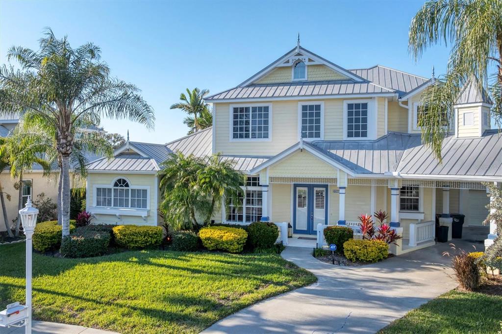 A two-story yellow house with a metal roof, palm trees, and a concrete driveway — 4627 BARRACUDA DRIVE, BRADENTON, FL