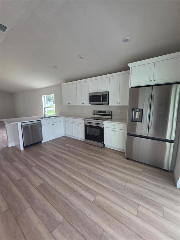 A modern kitchen features white cabinets, stainless steel appliances, and light wood-look flooring — 5346 SE 91ST STREET, OCALA, FL