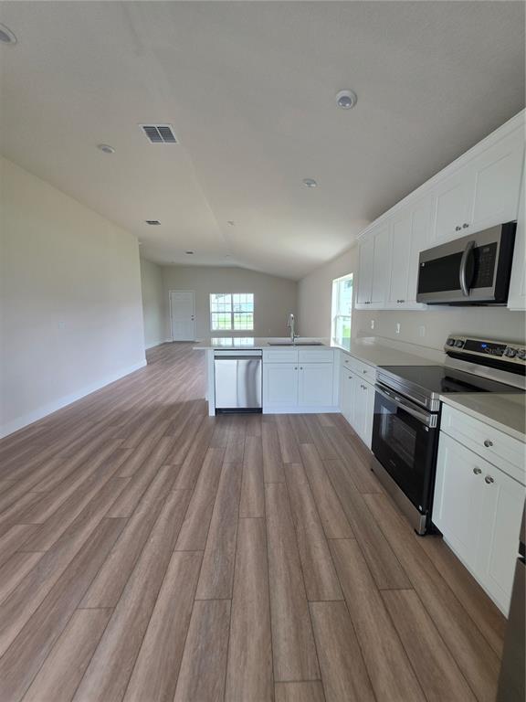 A kitchen with white cabinets and stainless steel appliances opens into a spacious living area — 5346 SE 91ST STREET, OCALA, FL