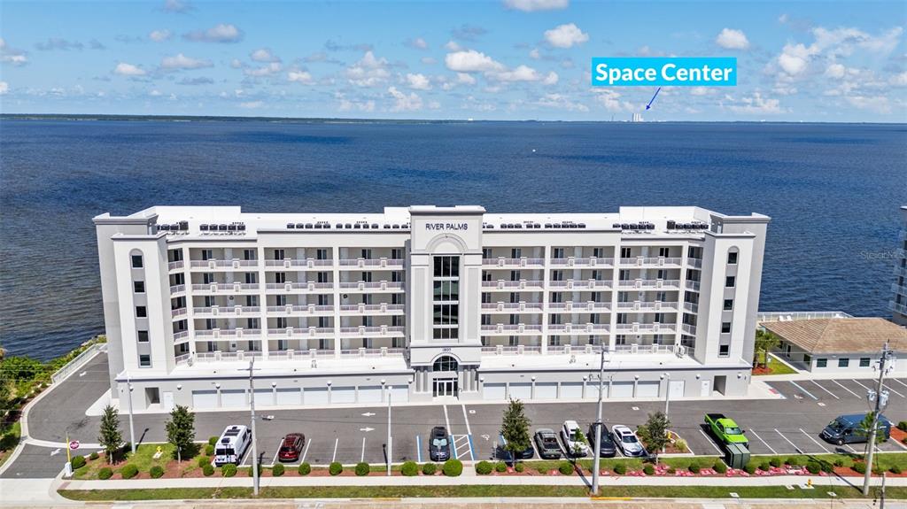 An aerial view shows a multi-story apartment building with balconies facing a large body of water — 1805 RIVERSIDE DRIVE UNIT 503, TITUSVILLE, FL