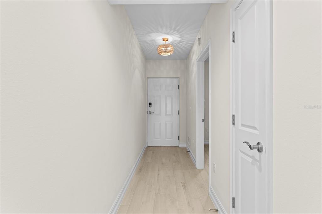 A narrow hallway with light wood flooring, white walls, and a decorative ceiling light fixture — 1805 RIVERSIDE DRIVE UNIT 503, TITUSVILLE, FL
