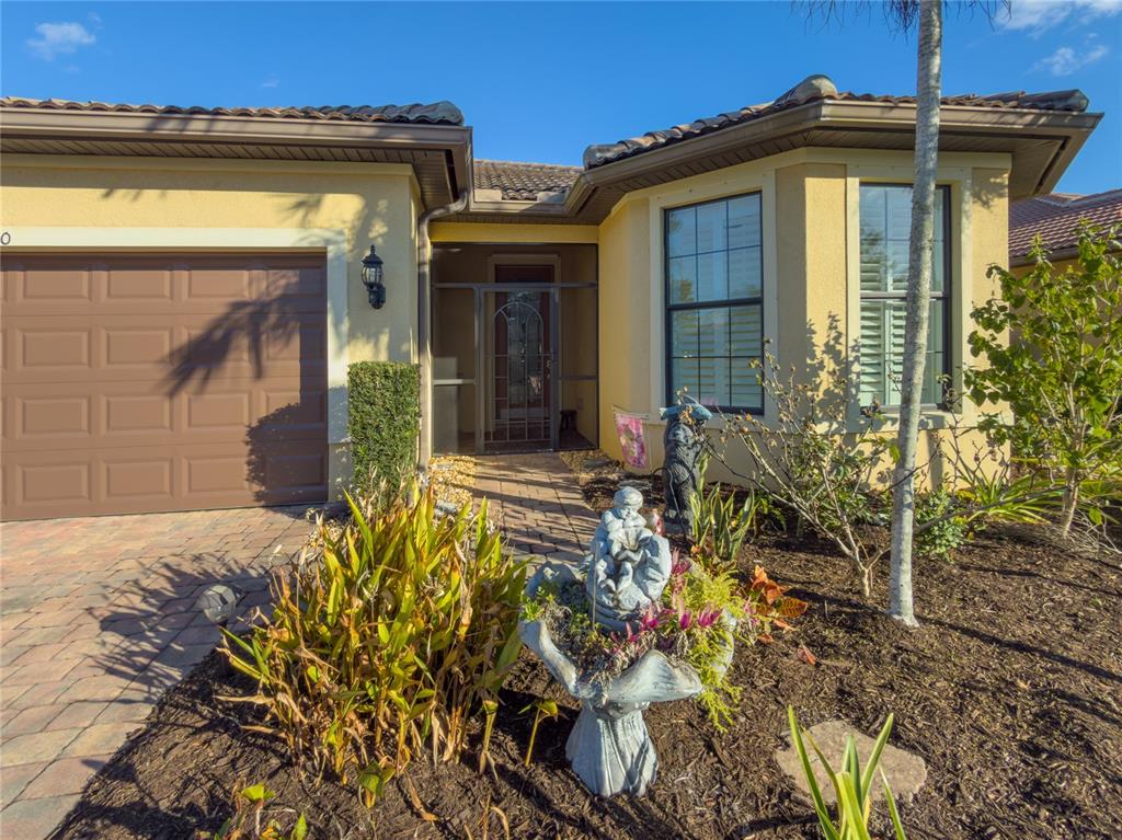 A yellow stucco house features a brown garage door, a screened entryway, and a garden — 19770 QUISTO STREET, VENICE, FL