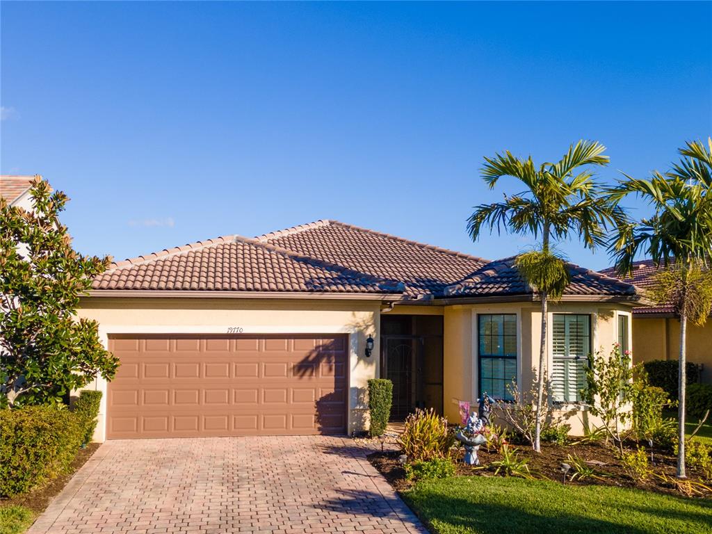 A single-story house with a brown tile roof, tan stucco walls, and a paved driveway — 19770 QUISTO STREET, VENICE, FL