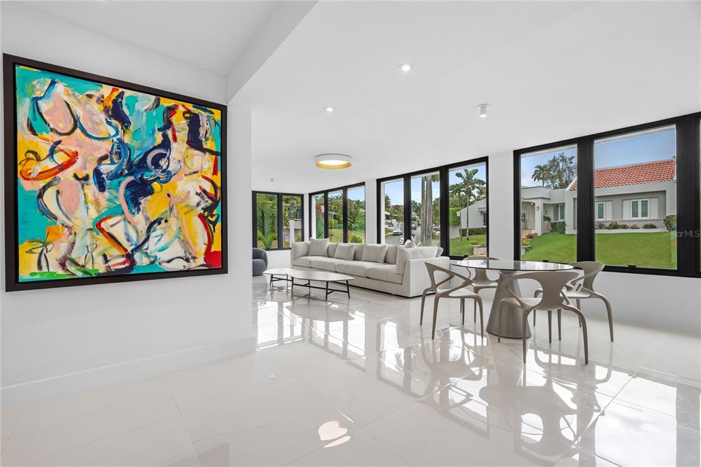 A modern living and dining area with white tile floors, large windows, and abstract art — D-1 SUN VALLEY, GUAYNABO, PR