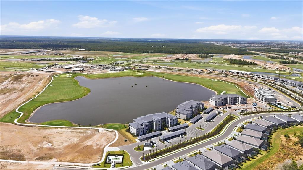 An aerial view shows a large lake surrounded by apartment buildings, golf course greens, and construction — 19140 SCALLOP LOOP UNIT 108, LAKEWOOD RANCH, FL