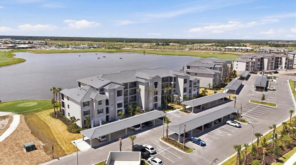 An aerial view shows a multi-story apartment building next to a lake and parking — 19140 SCALLOP LOOP UNIT 108, LAKEWOOD RANCH, FL