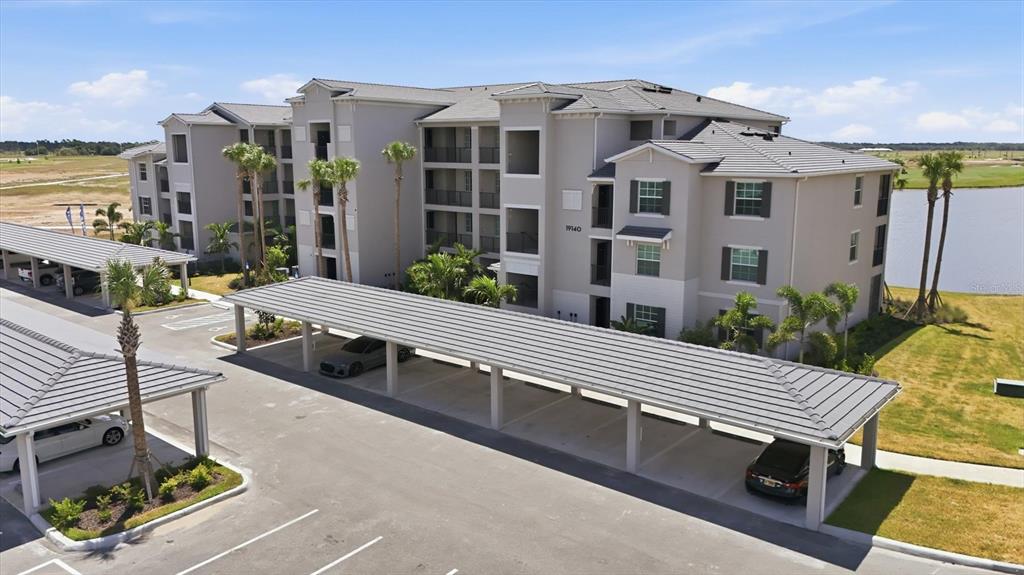 An aerial view shows a multi-story apartment building with covered parking spaces and palm trees — 19140 SCALLOP LOOP UNIT 108, LAKEWOOD RANCH, FL