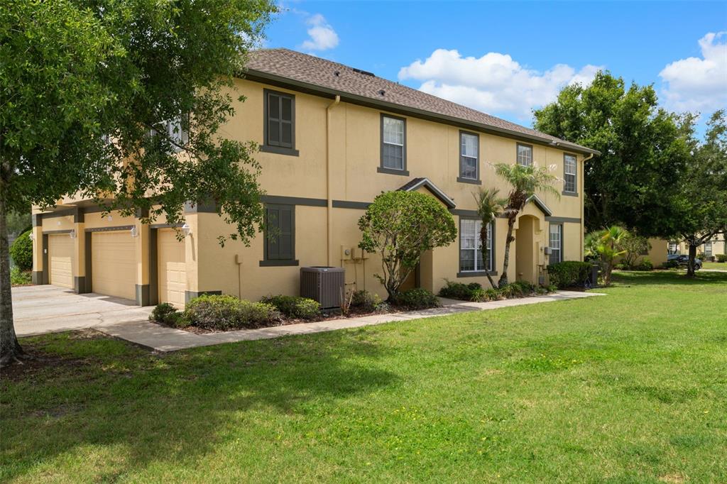 A two-story tan stucco townhouse with a multi-car garage and a grassy front lawn — 27642 PLEASURE RIDE LOOP, WESLEY CHAPEL, FL