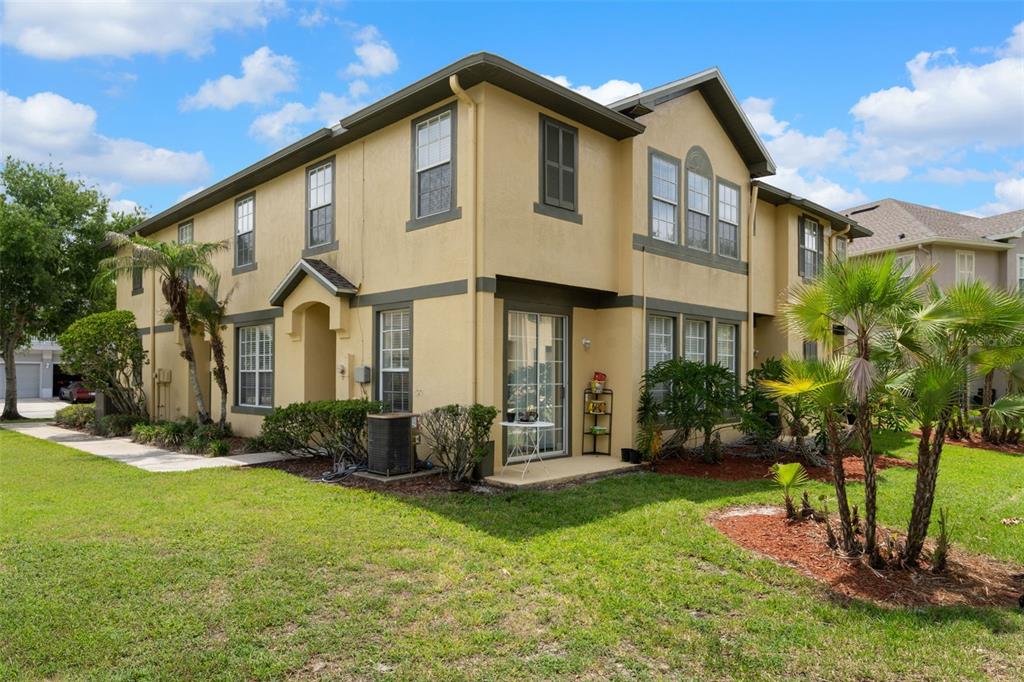 The exterior of a two-story tan stucco townhouse features a sliding glass door and landscaping — 27642 PLEASURE RIDE LOOP, WESLEY CHAPEL, FL