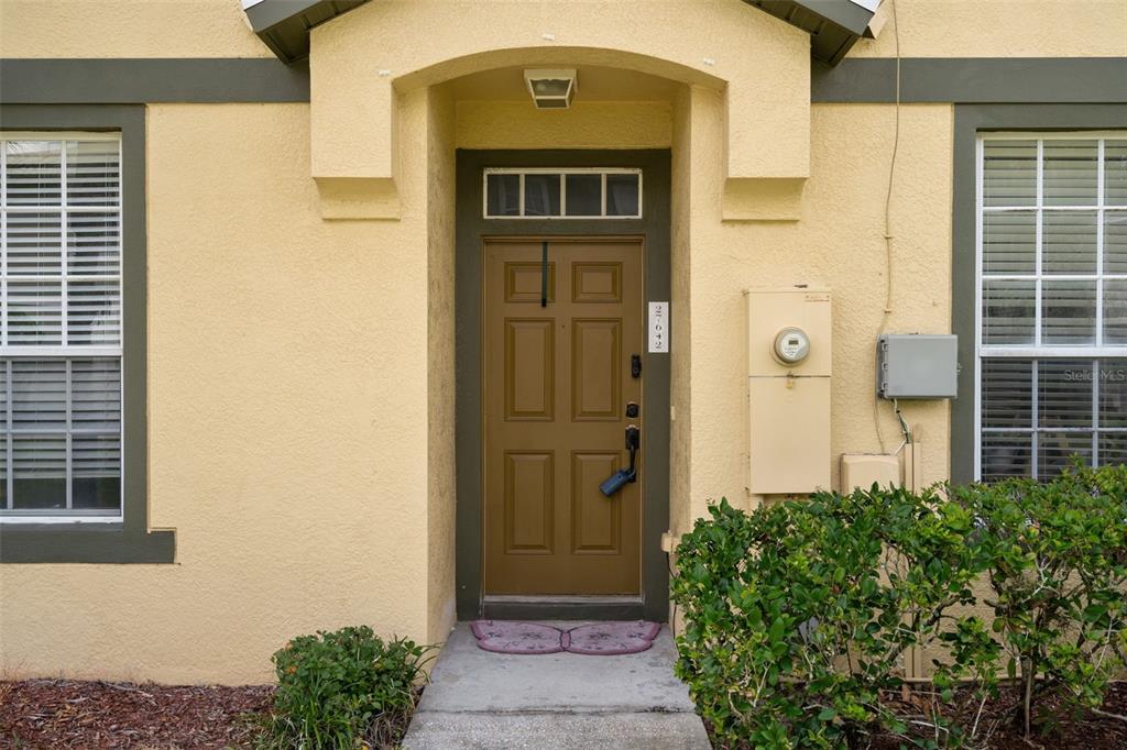 A tan house exterior features a brown front door with a lockbox and side windows — 27642 PLEASURE RIDE LOOP, WESLEY CHAPEL, FL