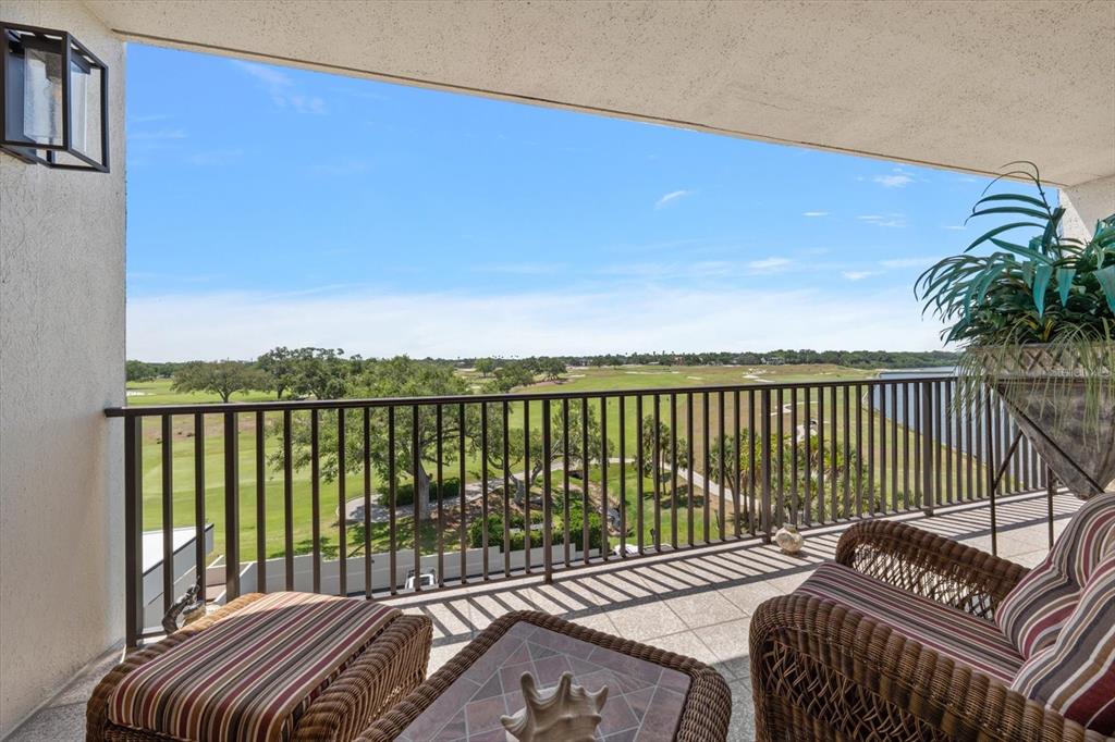 A balcony with wicker furniture overlooks a golf course and a body of water — 4 BELLEVIEW BOULEVARD UNIT 503, BELLEAIR, FL