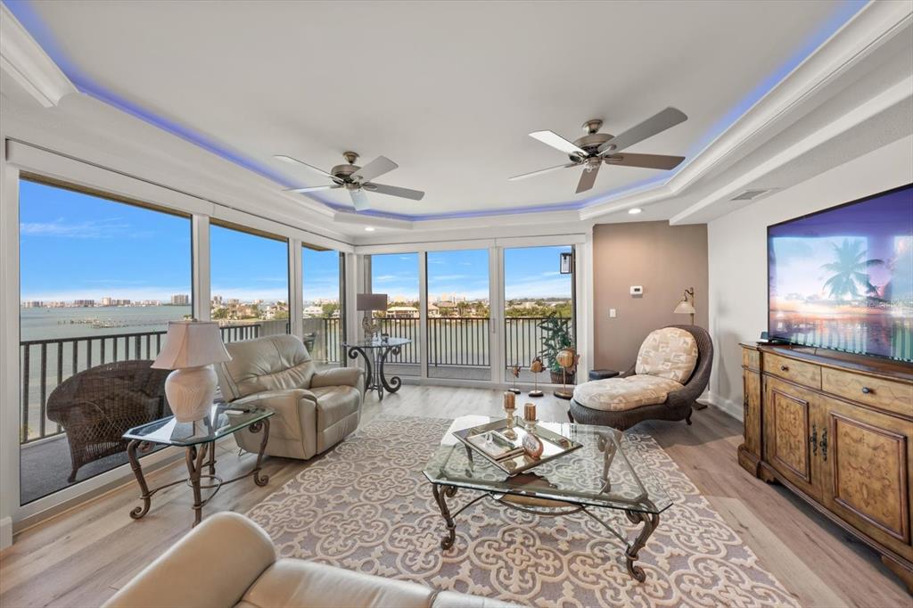 A living room with light wood floors, two ceiling fans, and floor-to-ceiling windows overlooking water — 4 BELLEVIEW BOULEVARD UNIT 503, BELLEAIR, FL