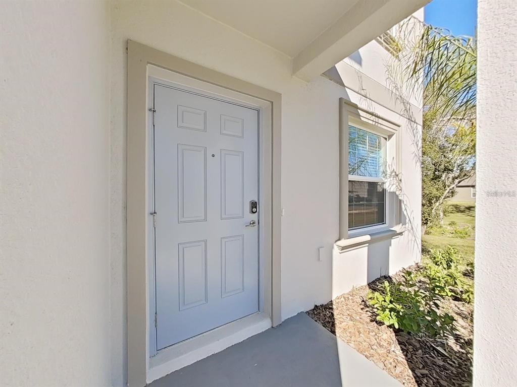 A light blue front door with a smart lock sits next to a window — 36385 FLATS STREET, ZEPHYRHILLS, FL