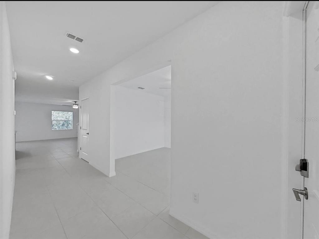 An interior view showing a white-walled hallway with tile flooring leading to an open room — 36385 FLATS STREET, ZEPHYRHILLS, FL