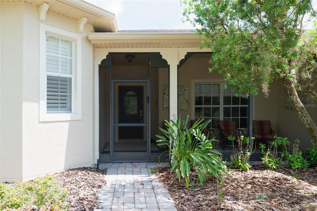 A paved walkway leads to the screened front entryway of a beige stucco house — 105 CUPOLA LOOP, KISSIMMEE, FL