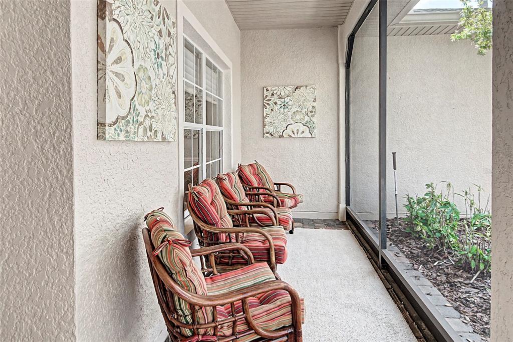 A screened-in patio features three wicker chairs with striped cushions and two floral wall canvases — 105 CUPOLA LOOP, KISSIMMEE, FL