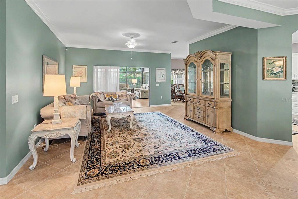 A living room with sage green walls, tile flooring, a large area rug, and a hutch — 105 CUPOLA LOOP, KISSIMMEE, FL