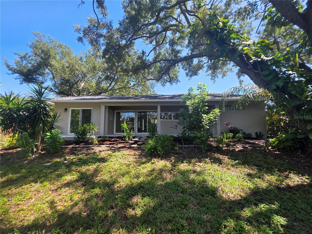 The exterior of a single-story house features a covered patio, sliding glass doors, and landscaping — 7708 NW 9TH AVE DRIVE, BRADENTON, FL